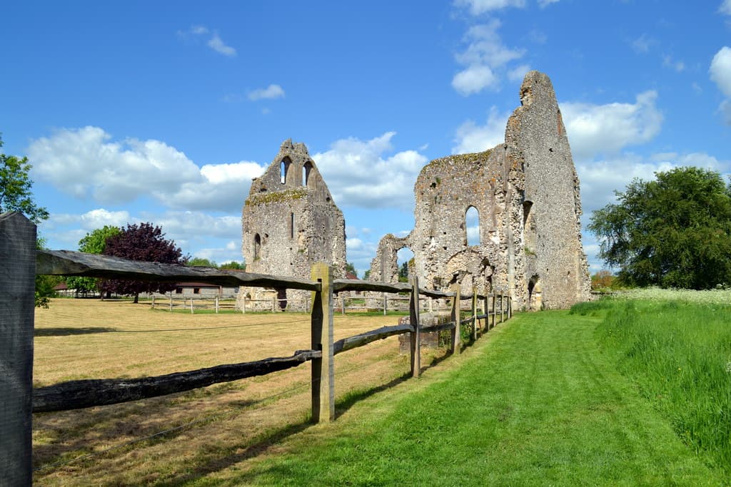 The tall roofless stone ruins of Boxgrove Priory guest house beyond a wooden fence and grass